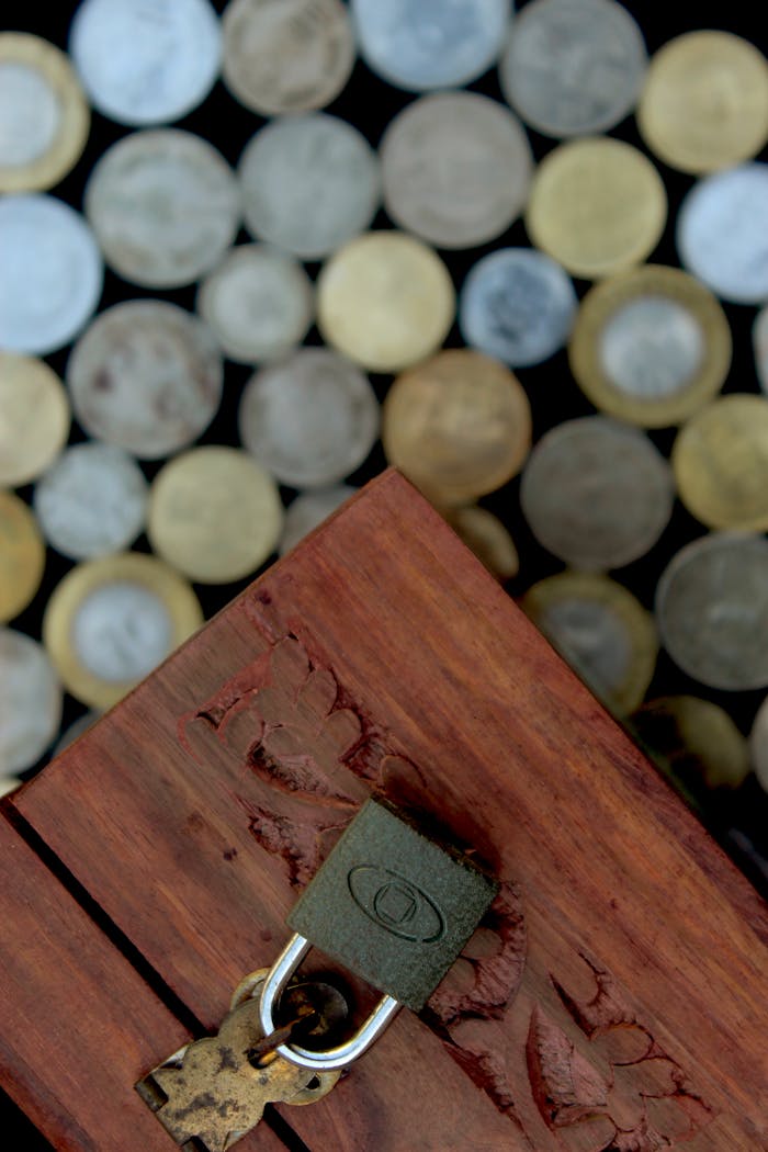 Top view of a locked wooden coin box surrounded by various currency coins, symbolizing savings and security.
