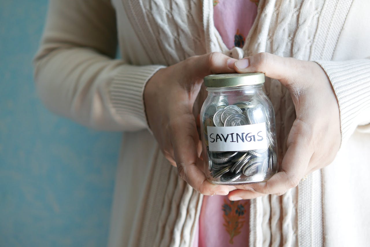 Woman holding a jar labeled savings filled with coins, representing financial savings.